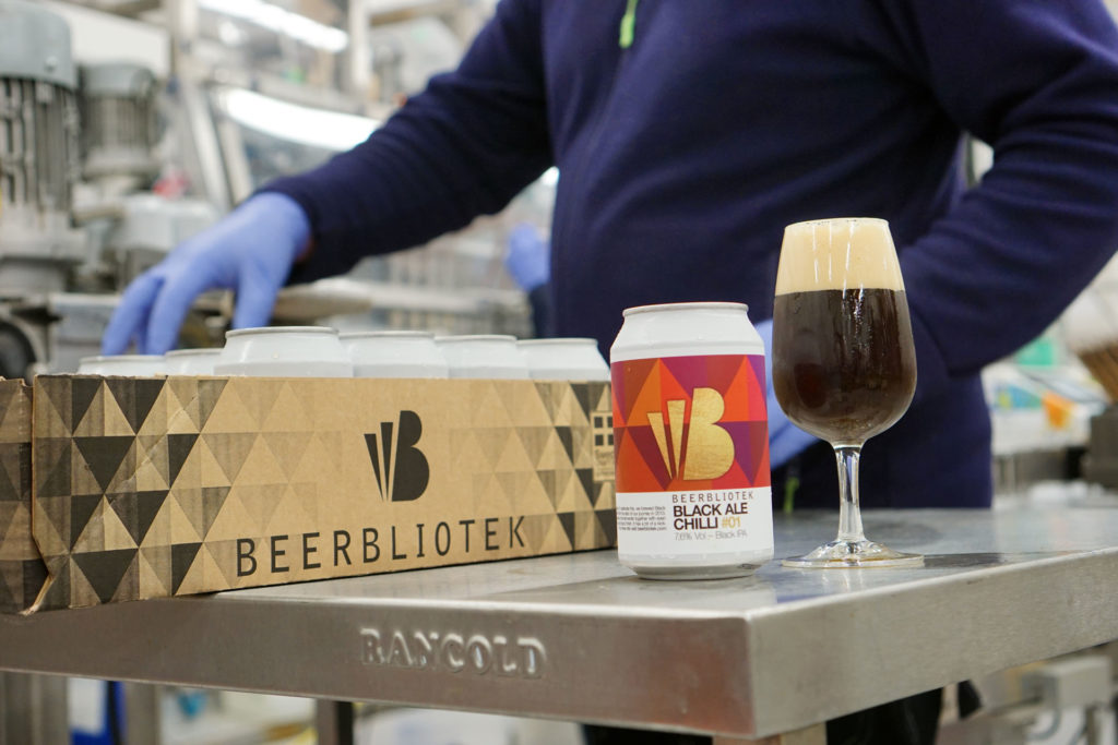 A can of Black Ale Chilli, the Black IPA from Beerbliotek Craft Brewery in Gothenburg Sweden next to a full glass of the same beer being tasted in the brewery during a packaging day.