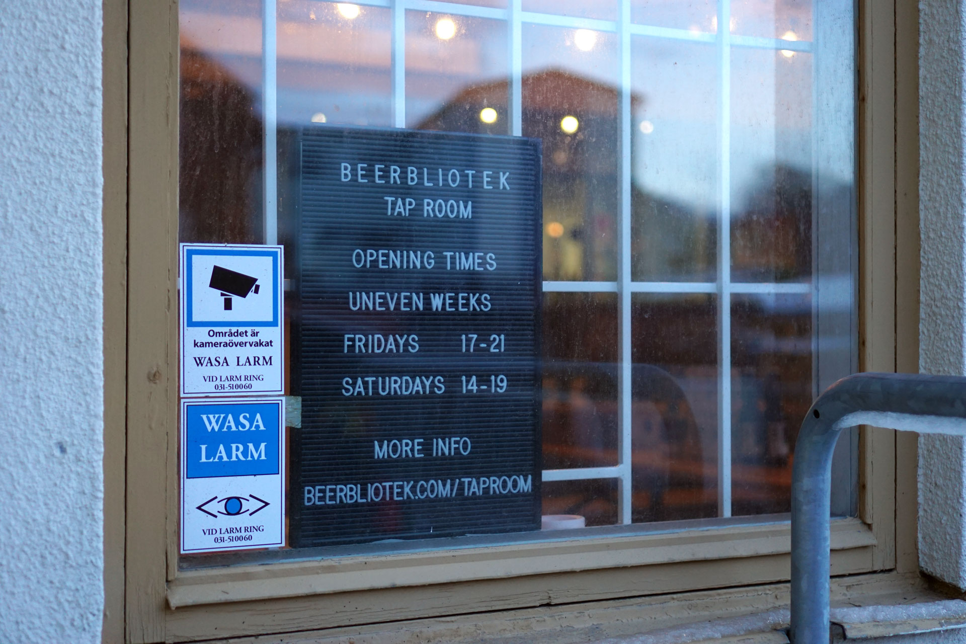 A sign with the opening times in the window of the Beerbliotek Tap Room in Gothenburg Sweden.